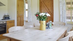 A wooden dining table with chairs, a vase with flowers, a coffee maker, and a wooden door in a kitchen.