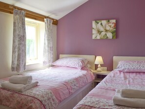 A bedroom with two beds, a window with curtains, a bedside lamp, and a floral painting on the wall.