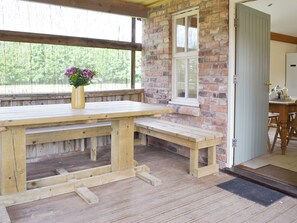 Una mesa de madera con bancos, un muro de ladrillo, una ventana y una puerta.