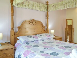 A bedroom with a four-poster bed, a nightstand with a lamp, a wooden dresser, and a mirror.