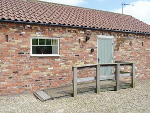 A brick building with a tiled roof, a window, a door, and a wooden deck.