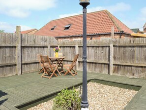 A wooden deck with a table and chairs, a wooden fence, and a building with a red roof in the background.