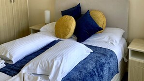A neatly made bed with white and blue bedding, two pillows, and a blue blanket.