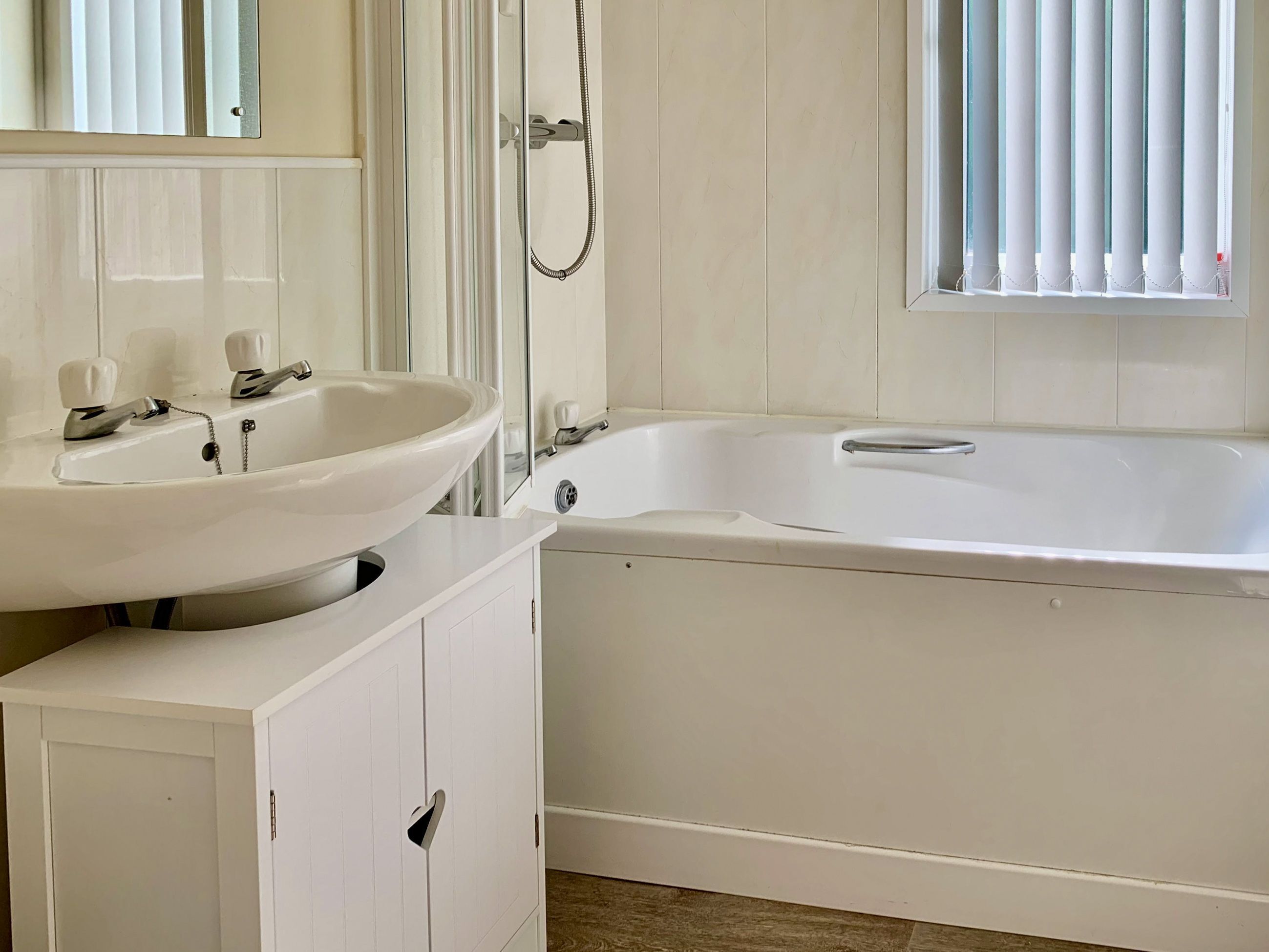 A bathroom with a white sink, a bathtub, and a window with blinds.