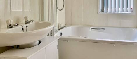 A bathroom with a white sink, a bathtub, and a window with blinds.