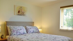 Een slaapkamer met een bed, twee nachtkastjes, een lamp, een schilderij aan de muur en een raam met jaloezieën.