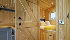 Een houten interieur met een bed, een raam en een deur met een handgreep.