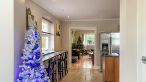 Une cuisine avec un réfrigérateur blanc, des meubles en bois, un coin repas avec un bar et un sapin de Noël.