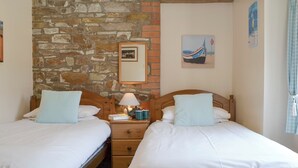 Une pièce avec deux lits en bois, un mur en pierre, une table de chevet avec une lampe et un tableau encadré accroché au mur.