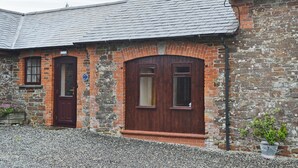 Un bâtiment doté d’une façade en pierre, de deux portes en bois et d’une allée gravillonnée.