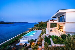 A modern house with a swimming pool, overlooking a large body of water and hills. - Villas Anita (Zadar)