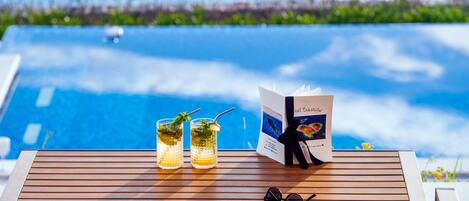 A wooden table with two glasses of a beverage, a brochure, and a pair of sunglasses.