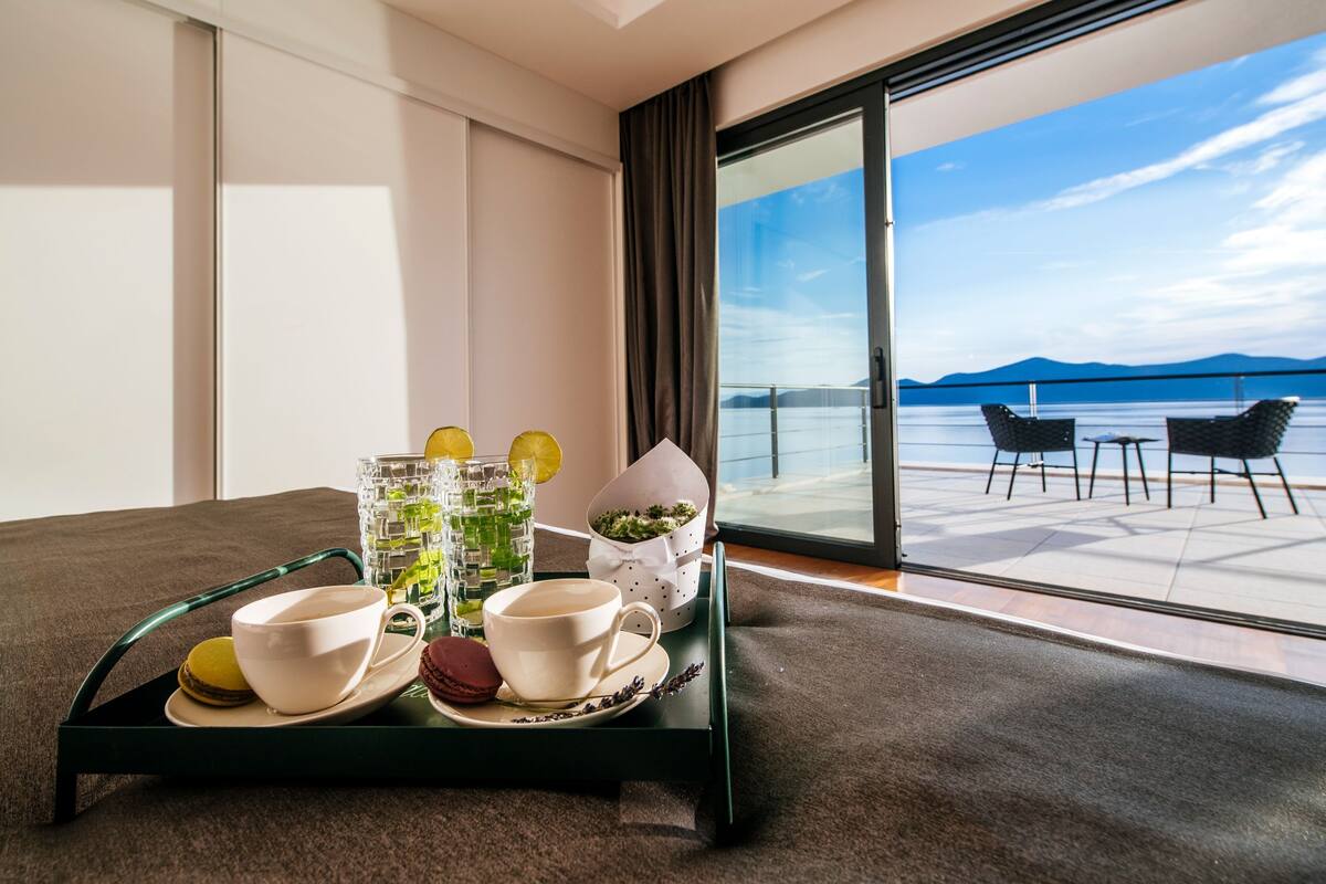 A room with a balcony, a tray with a cup, a glass of water, and a bowl of macarons.