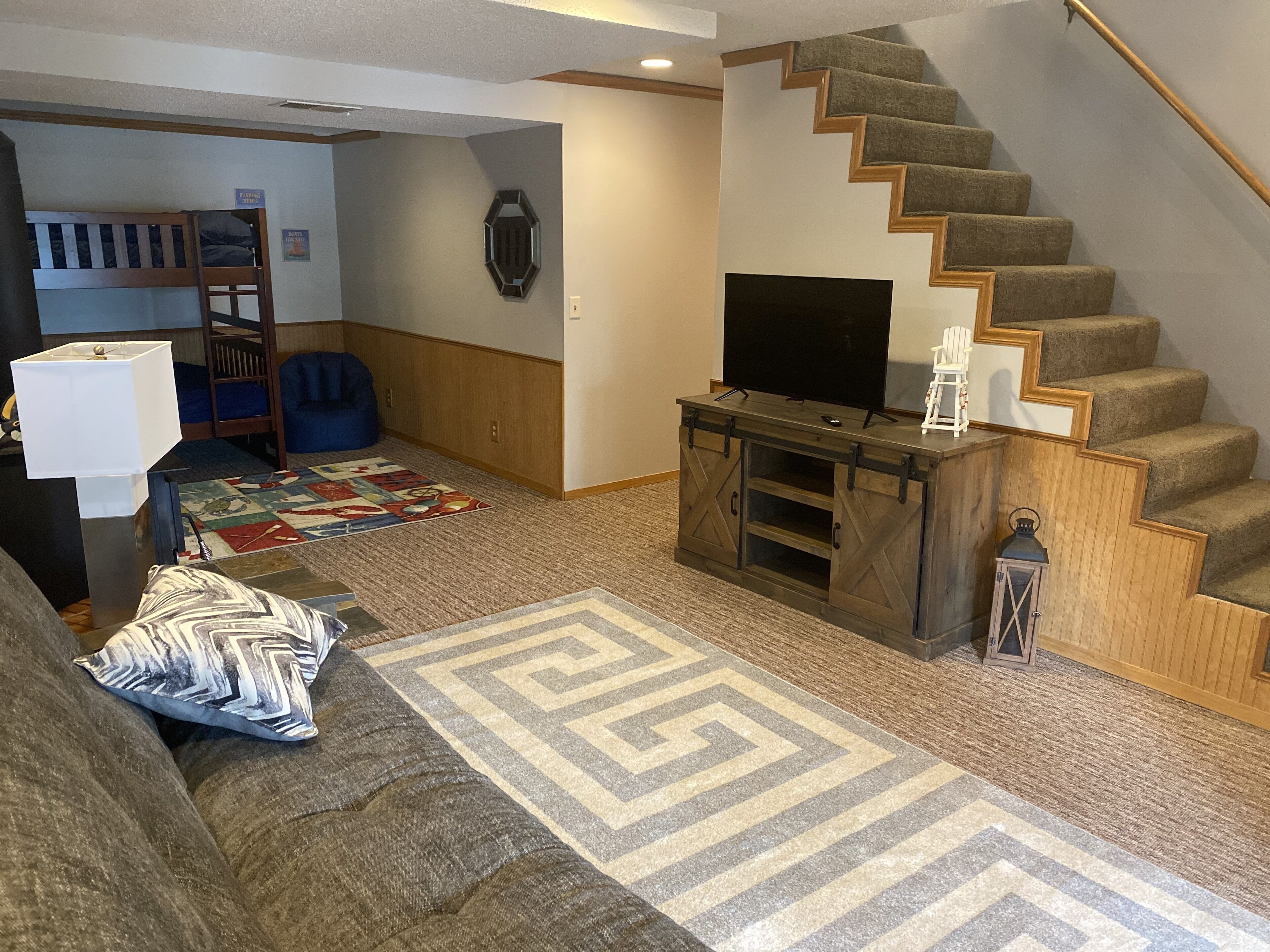 Una sala de estar con una escalera, un televisor sobre un mueble de madera, un sofá y una alfombra.