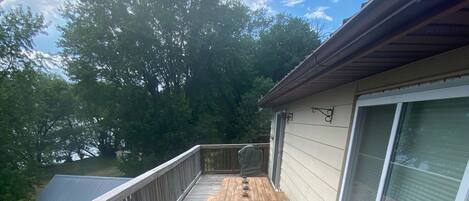 A deck with a wooden table and chairs, a cushioned bench, and a covered grill area.