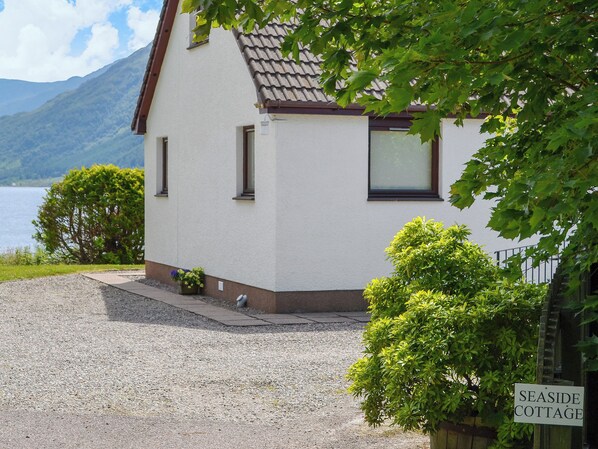 Ein weißes Gebäude mit einem braunen Dach, einer Schotterauffahrt und einem Schild mit der Aufschrift 'SEASIDE COTTAGE'.
