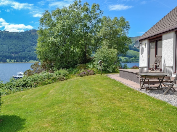 A lakeside property with a grassy lawn, a patio with outdoor furniture, and a view of the lake and mountains.