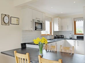 A modern kitchen with white cabinets, a built-in microwave, a coffee machine, and a dining area with a table and chairs.