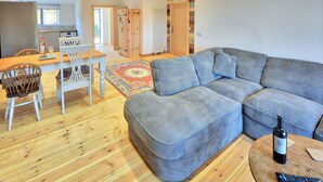 Una sala de estar con un sofá modular, un comedor con mesa y sillas de madera, y una cocina al fondo.