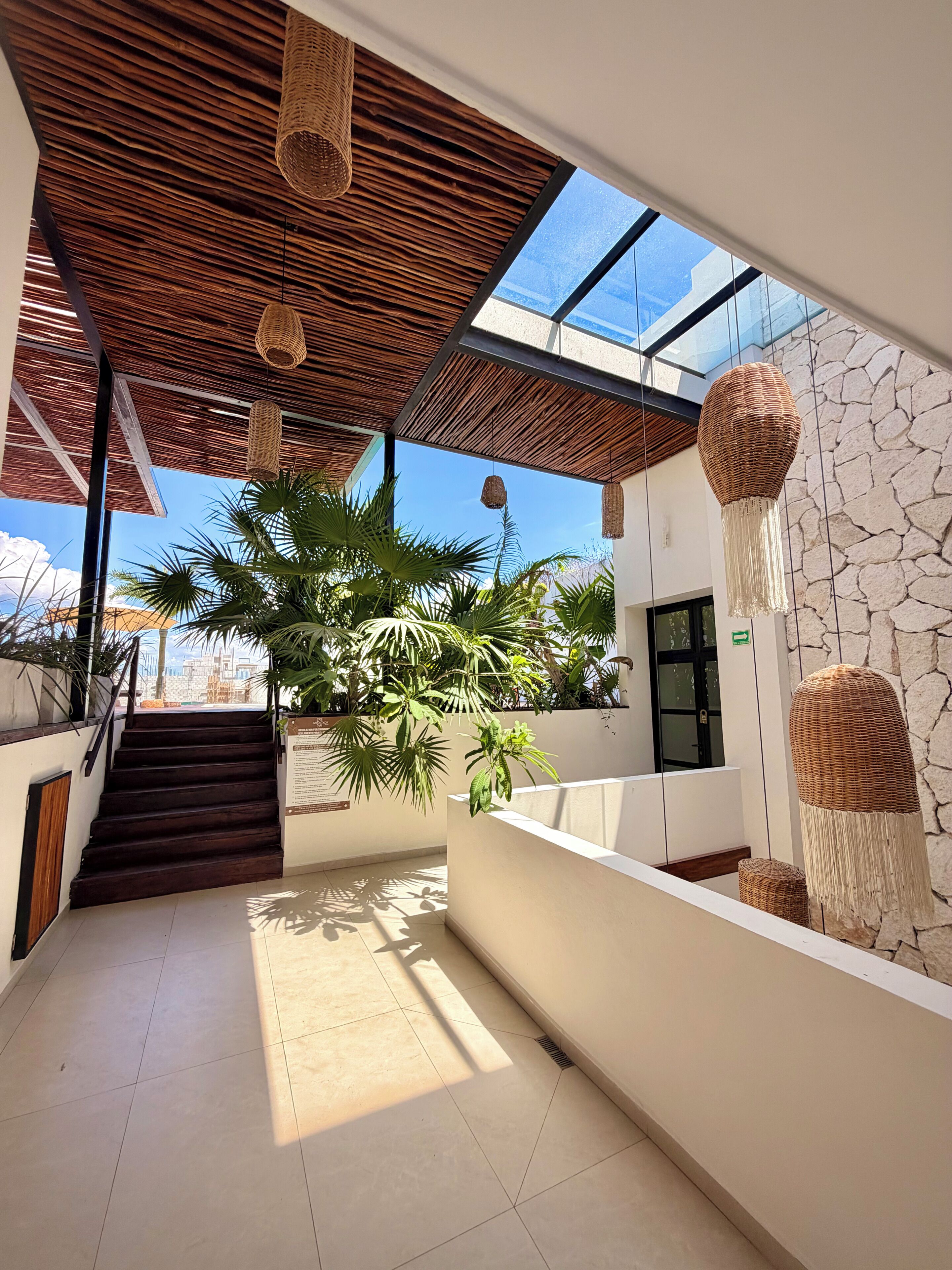 Un interior moderno con una escalera, techo de vidrio y pared de piedra.