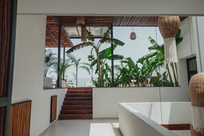 Ein modernes Interieur mit einer Treppe, die zu einem Balkon mit Blick auf üppiges Grün und das Meer führt.