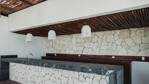 Una encimera de piedra con un grifo, vigas de techo de madera y luces colgantes.