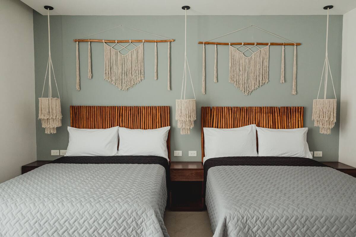 Habitación doble con dos camas, cabeceros de madera, tapices de macramé y una paleta de colores neutros.