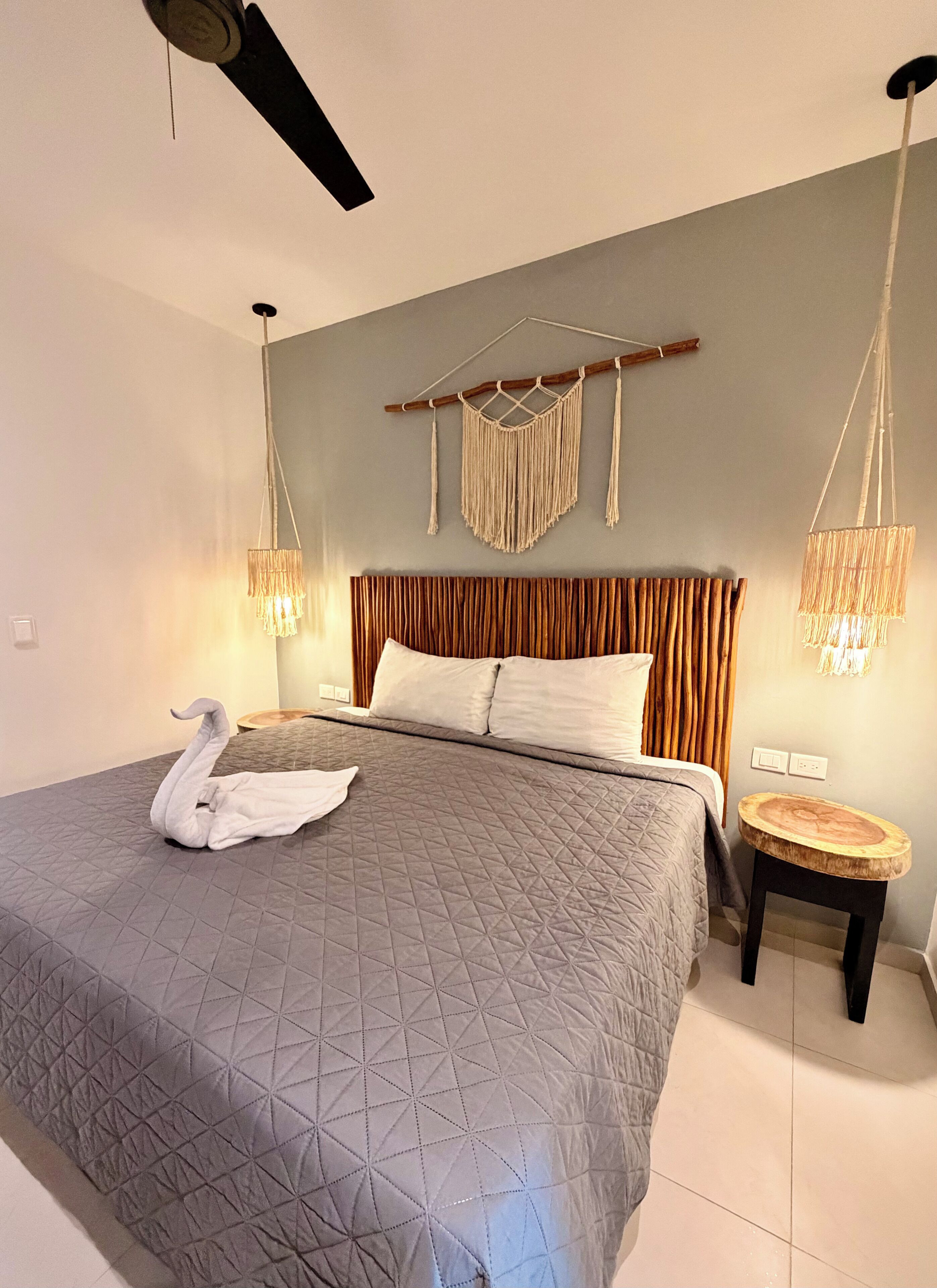 Een net opgemaakt bed met een sprei met een geometrisch patroon, een houten hoofdbord en een macramé wanddecoratie.