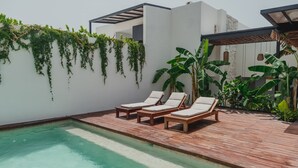 Zona de piscina con terraza de madera y sillones reclinables, rodeada de vegetación y arquitectura moderna.