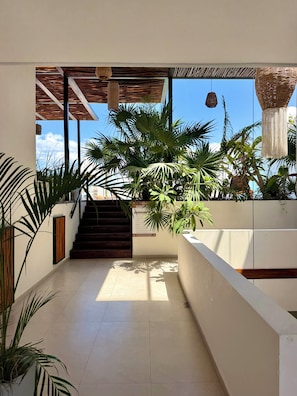 A modern interior with a staircase leading to a balcony, surrounded by lush tropical plants and a clear view of the sky. - Ah Xok suites 5a Avenida (Playa del Carmen)
