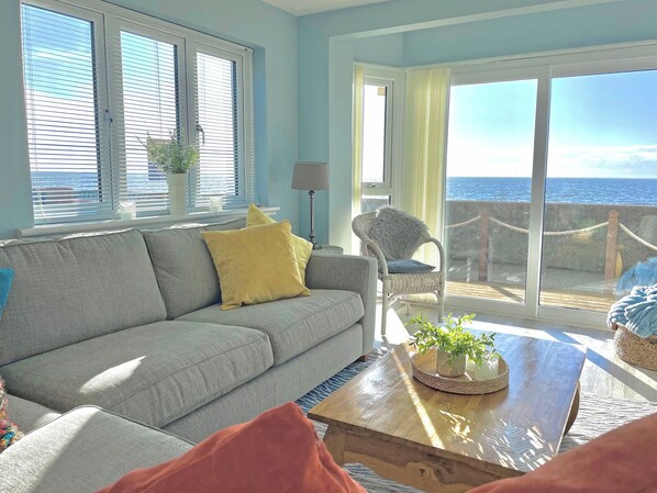 A living room with a sofa, a chair, a coffee table, and a view of the sea through large windows. - 4 bedroom accommodation in Point Clear, near Clacton-on-Sea (Point Clear, near Clacton-on-Sea)