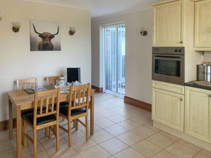 A dining area with a wooden table and chairs, a kitchen with cabinets and an oven, and a sliding glass door leading to a balcony.