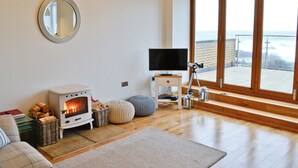 Een gezellige woonkamer met een houtkachel, een flatscreen televisie en een groot raam met uitzicht op een balkon.