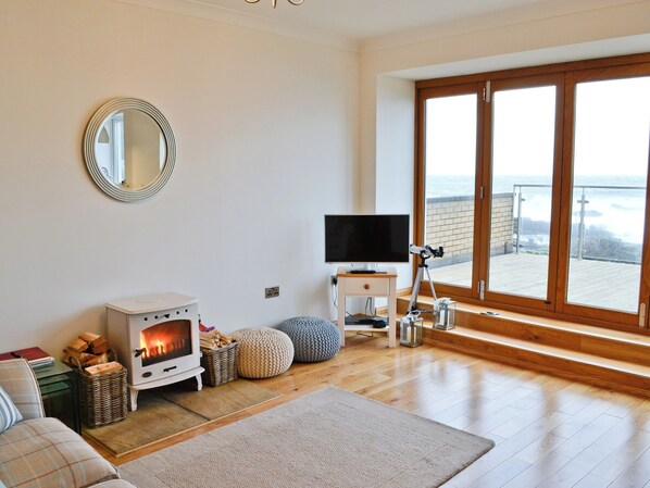 A cozy living room with a wood-burning stove, a flat-screen TV, and a large window overlooking a balcony.