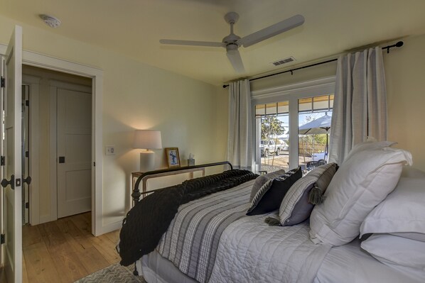 Ein Schlafzimmer mit Bett, Deckenventilator, Fenster mit Vorhängen und einer Tür zu einem anderen Raum.