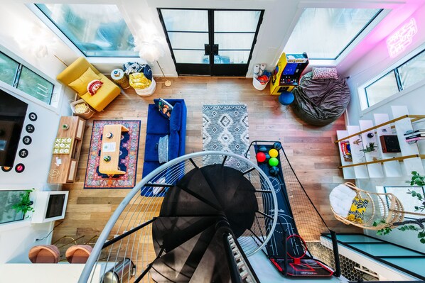 Un loft spacieux doté d’une grande verrière, d’un canapé bleu, d’un fauteuil jaune, d’un pouf et d’un petit coin repas.