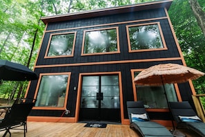 Uma cabana de dois andares com janelas amplas, um deck e área de estar externa.