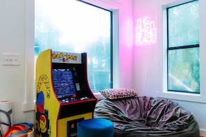 Quarto com uma máquina de arcade Pac-Man, uma poltrona de saco de feijão e um letreiro neon.