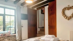 Quarto com cama, duas toalhas, um enfeite em formato de coração, uma janela e uma porta que dá para uma escadaria.