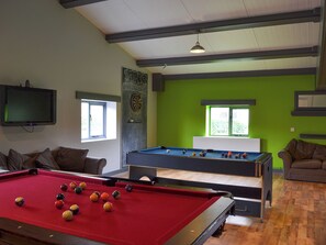 A pool table with balls, a television, and a dartboard in a room with green walls and windows.