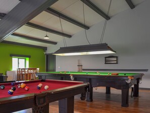 A pool hall with two pool tables, chairs, and a green wall.
