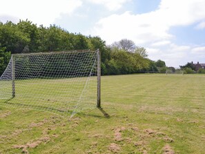 A soccer goal on a grassy field with trees in the background.