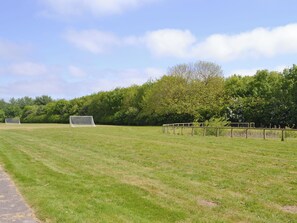 A grassy field with two soccer goals and a wooden fence.