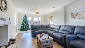 Un salon moderne avec un canapé d’angle, une petite table basse en bois, un sapin de Noël et une cheminée.