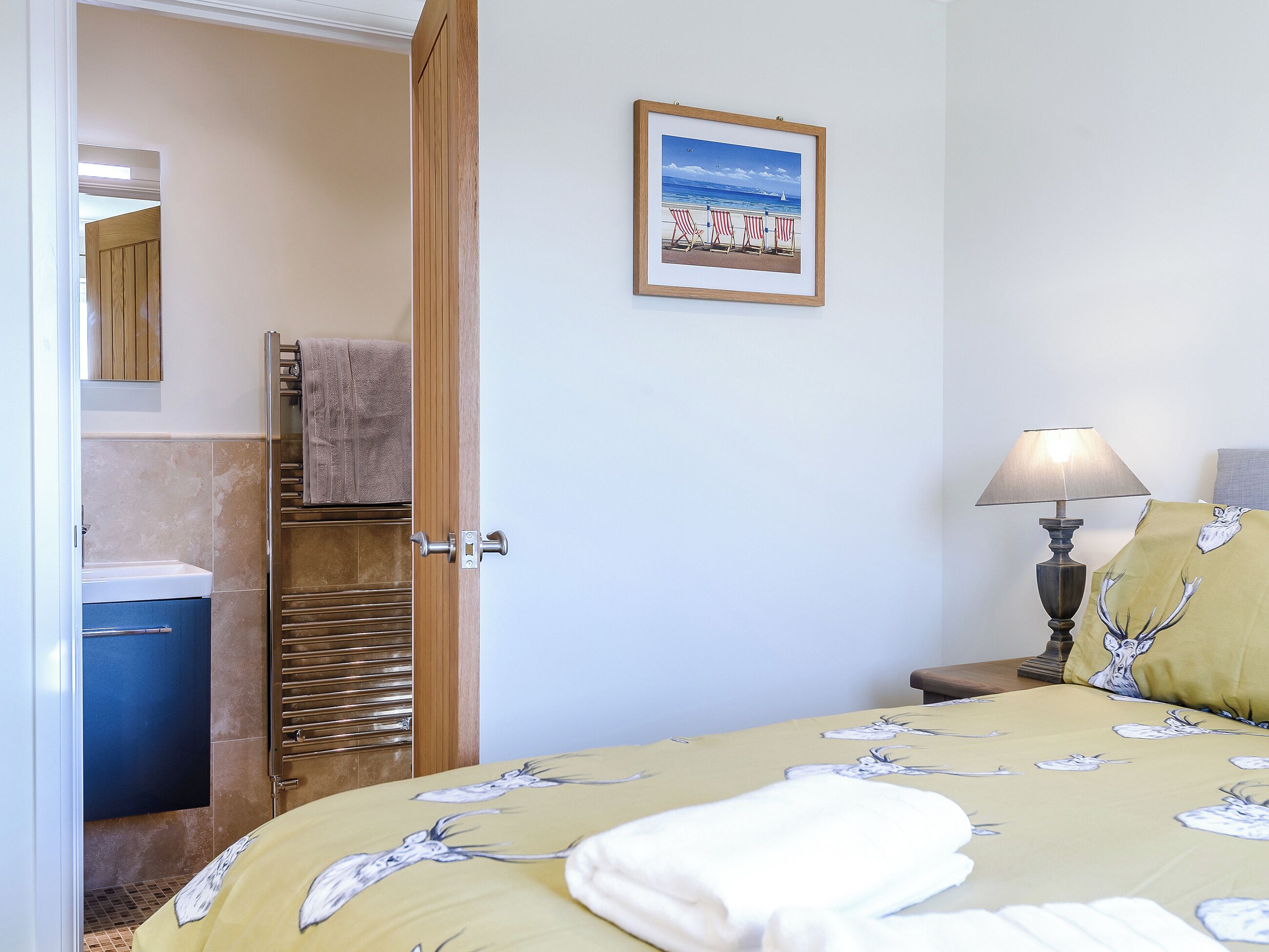 Ein Hotelzimmer mit Bett, Nachttischlampe, Handtuch, einem gerahmten Bild und einem durchgegangenes Badezimmer.