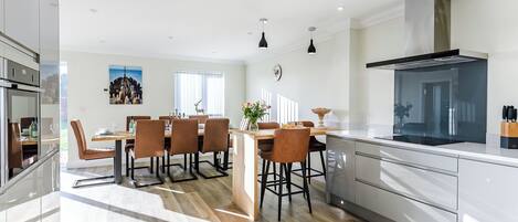 A modern kitchen with a central island, a dining area with chairs, and a large window.