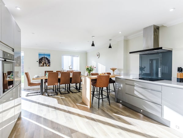 A modern kitchen with a central island, a dining area with chairs, and a large window.