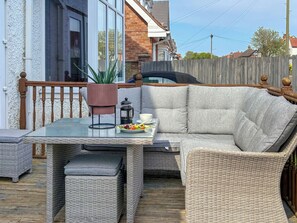 A wicker outdoor seating area with a table, cushions, a potted plant, and a lantern.