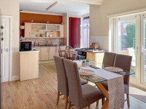 A modern kitchen with wooden cabinets, a dining area with a glass table and chairs, and a view of the outside through a sliding glass door.