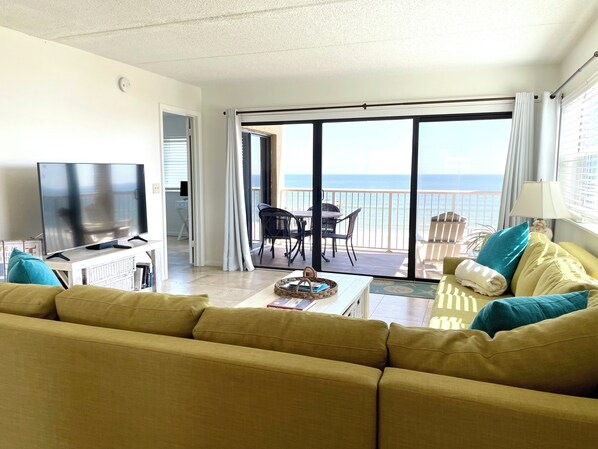 A living room with a sofa, a TV, and a balcony with a view of the sea. - Oceanfront Top-Floor Corner Unit, Fishing Pier & Pool at Amelia By The Sea (Fernandina Beach)
